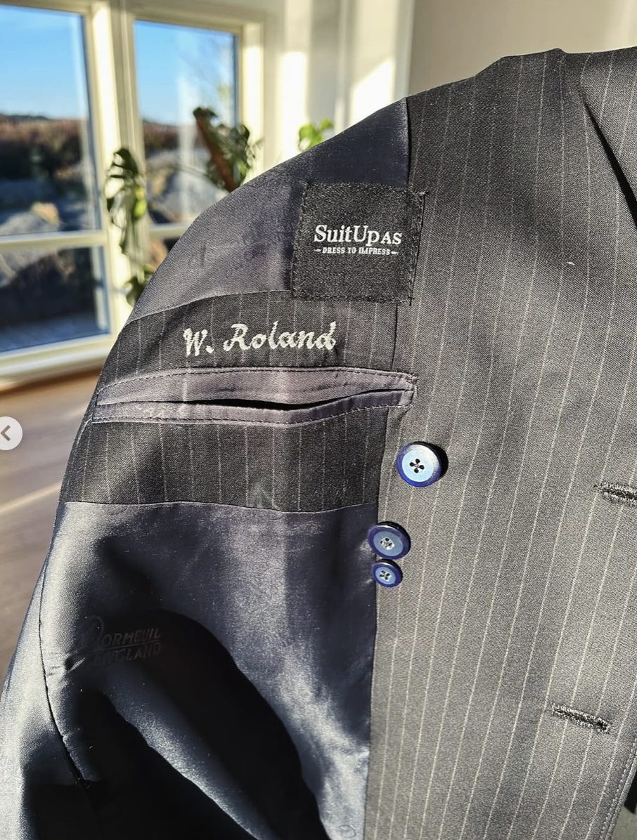 Detaljbilde av innside på pinstripe-dress med blå knapper og brodert navn