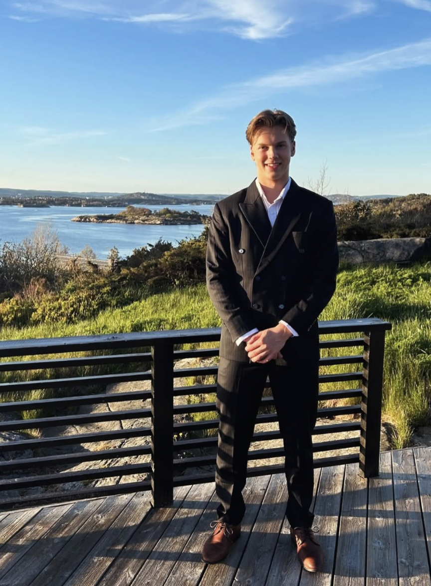 SuitUp-kunde i mørk dobbelspent dress ved kysten i kveldssol