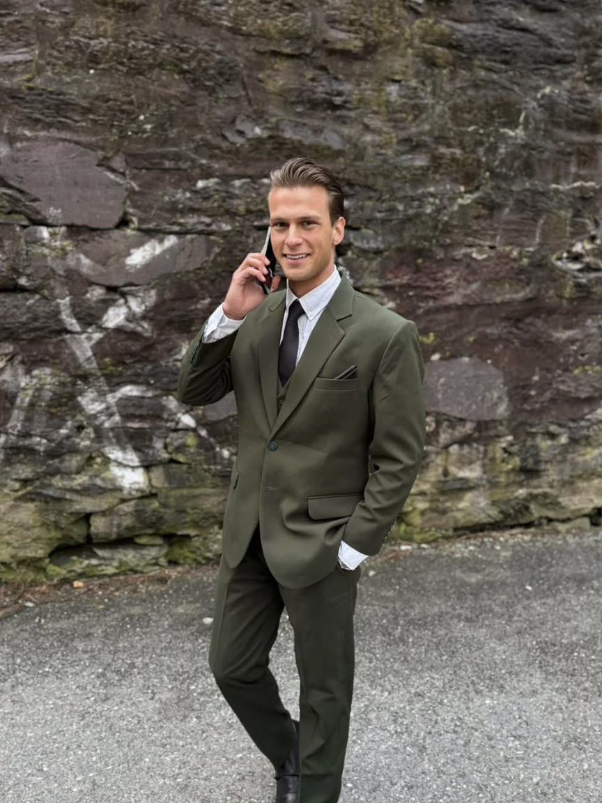 SuitUp-kunde i olivengrønn dress mot steinmur